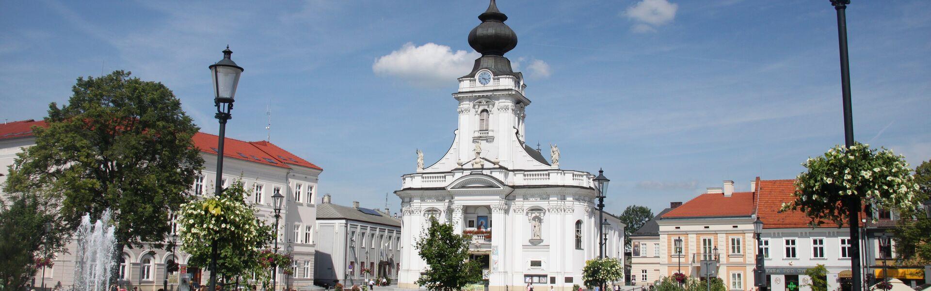 Rynek w Wadowicach, widok na biały kościół i plac przed nim i kamienice, spacerujący ludzie